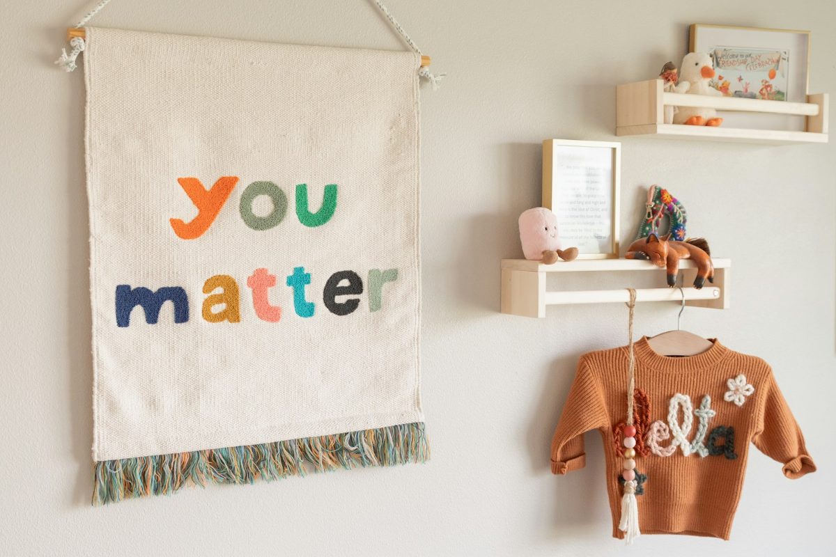 Stoff-Wandbehang mit Schriftzug und kleines Wandregal im Kinderzimmer