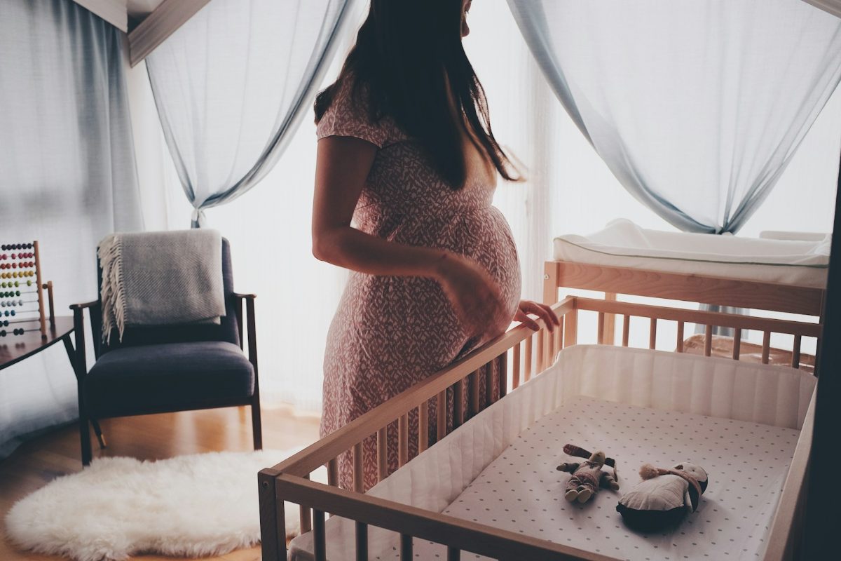 Schwangere Frau steht vor einem fertig eingerichteten Gitterbett im Babyzimmer