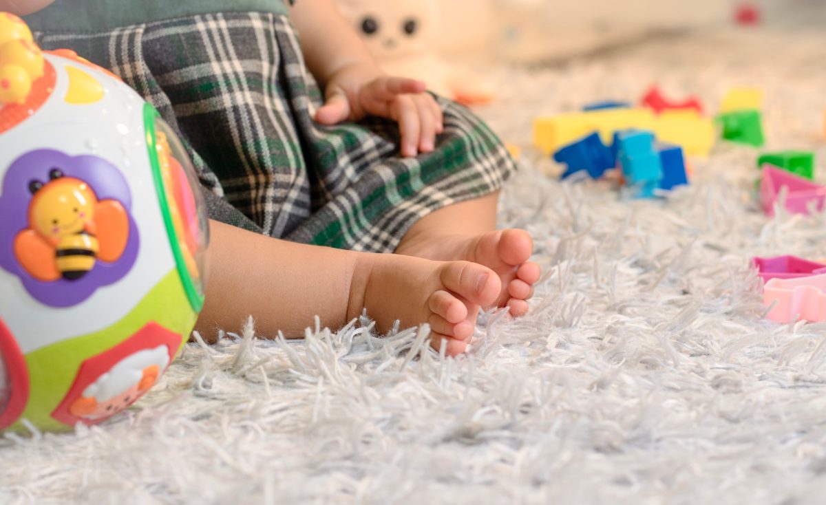 Baby sitzt auf einem weichen hochflorigen Kinderteppich und spielt mit Bausteinen