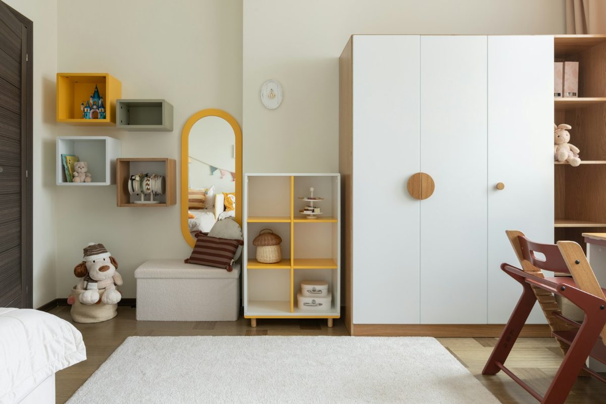 Kinderzimmer mit weissen Moebeln und gelben Farbakzenten an Regal und Deko