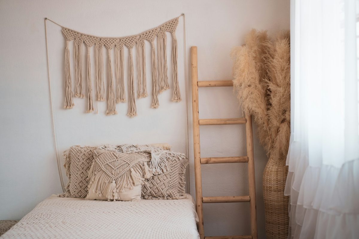 Makramee-Wandbehang und Holzleiter ueber einem Bett mit Strickdecke